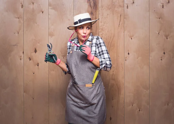 Elinde budama makası tutan genç bahçıvan kadın stüdyodaki ahşap arka planda fısıldıyor. Gizli bilgi. Stüdyo çekimi