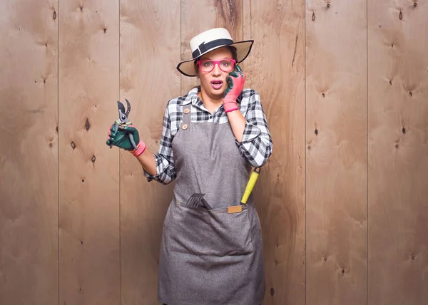 Yanlışlık. Elinde budama makası tutan ürkek genç bahçıvan kadın stüdyoda ahşap arka planda sana bakıyor. Stüdyo çekimi