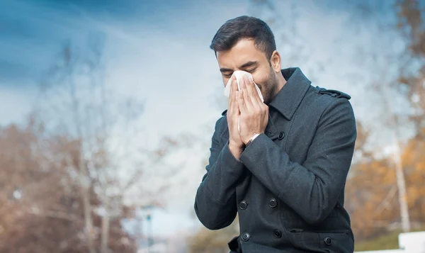 Un hombre sonándose la nariz en un parque. Al aire libre, al exterior . — Foto de Stock