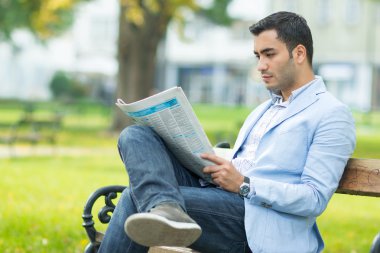 Bankta oturan ve gazete okuyan genç işadamı
