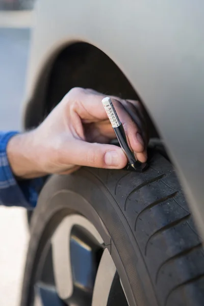 Nahaufnahme eines Mannes, der die Lauffläche eines Autoreifens mit Messgerät überprüft — Stockfoto