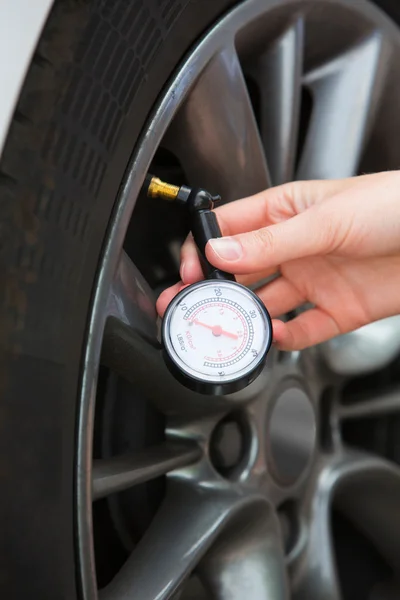 Close-up de mulher verificando a pressão do pneu do carro com calibre — Fotografia de Stock