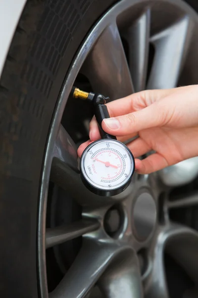 Nahaufnahme einer Frau, die mit Messgerät den Reifendruck ihres Autos überprüft — Stockfoto