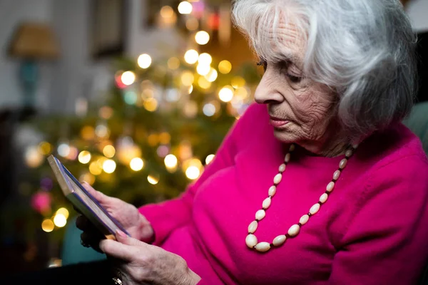 Sad And Lonely Senior Woman Spending Christmas At Home Alone Looking At Family Photograph