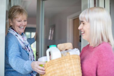 Kadın komşu, evden alışveriş yaparak kıdemli kadına yardım ediyor.