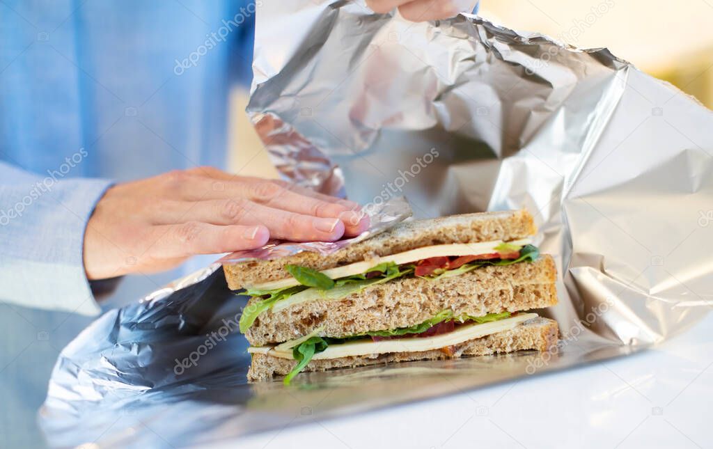 Close Up Of Woman Wrapping Sandwich In Non Reusable Aluminium Foil