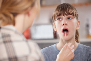 Anne, kızına hızlı bir Lateral Akış Testi uyguluyor.