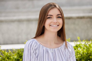 Kampüsün dışında oturan gülümseyen genç kız öğrenci portresi.