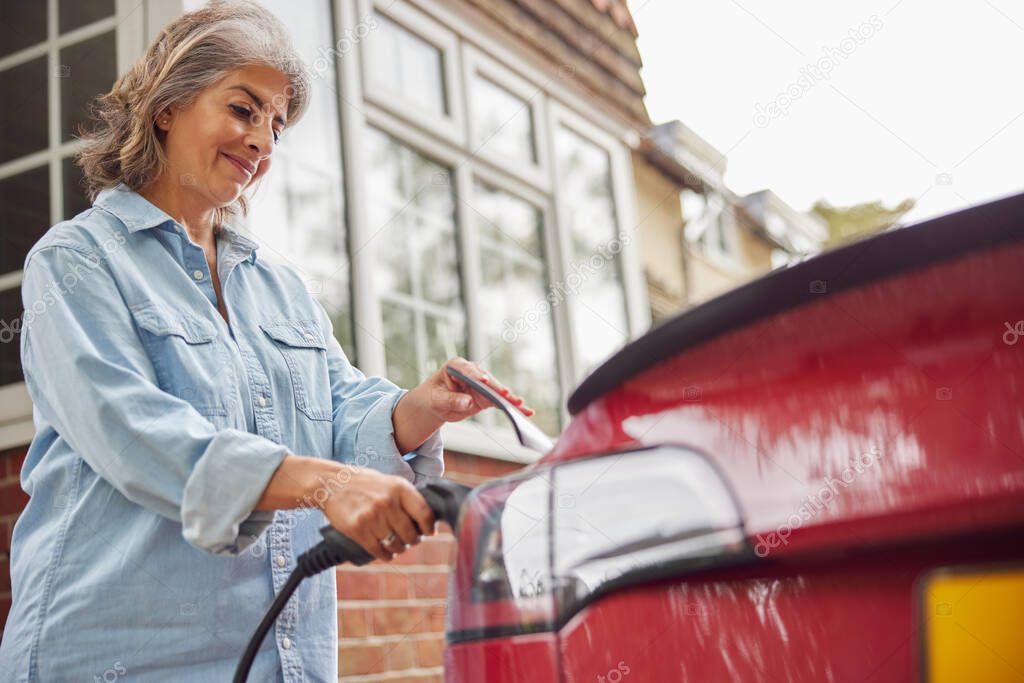 Mature Woman Attaching Charging Cable To Environmentally Friendly Zero Emission Electric Car At Home