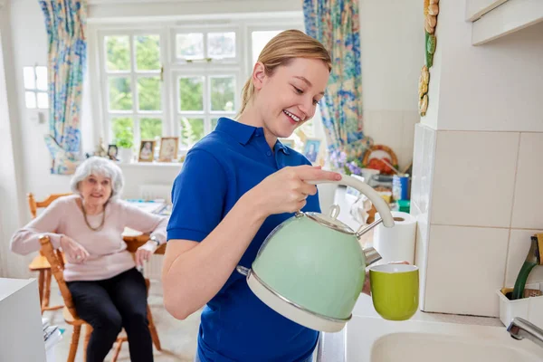 Γυναίκα Home Help Making Cup Tea Kitchen While Chatting Senior — Φωτογραφία Αρχείου