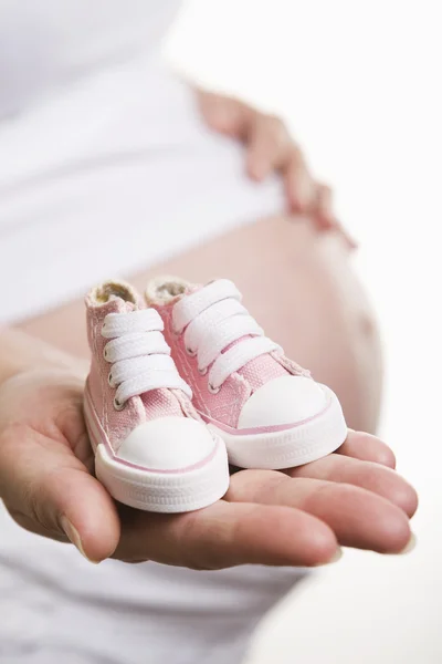 Mujer embarazada sosteniendo zapatos de bebé — Foto de Stock