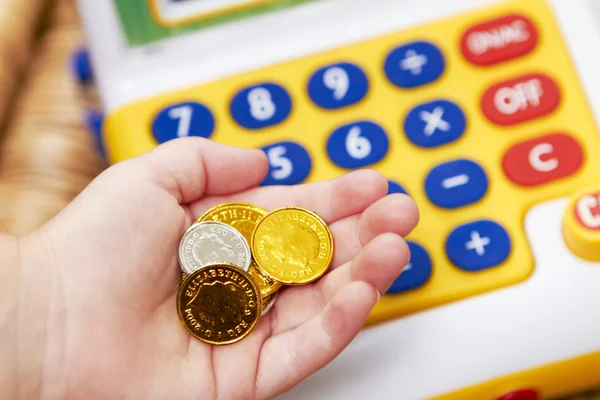 Child's Hand Holding Pretend Coins Next To Toy Cash Register — Stock Photo, Image