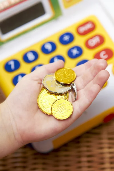 Child's Hand Holding Pretend Coins Next To Toy Cash Register — Stock Photo, Image