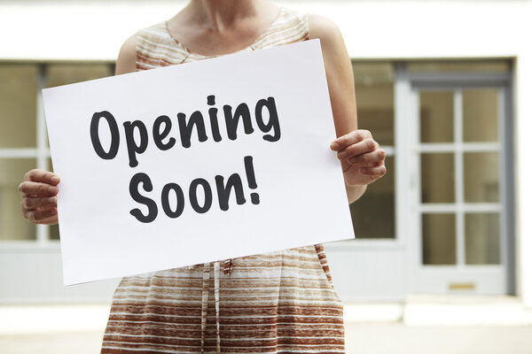 Woman Standing Outside Empty Shop Holding Opening Soon Sign