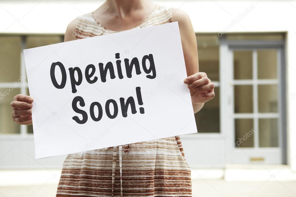 Woman Standing Outside Empty Shop Holding Opening Soon Sign
