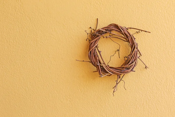 Милий плетений дерев'яний вінок з висушеної гілки, що звисає на жовтій стіні — стокове фото