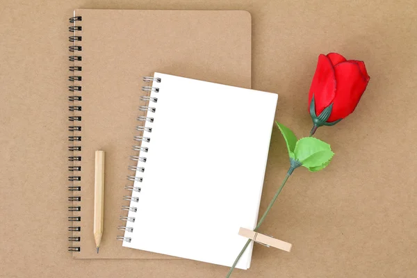 Чистый блокнот на натуральной коричневой бумаге рядом с деревянным карандашом и розой — стоковое фото