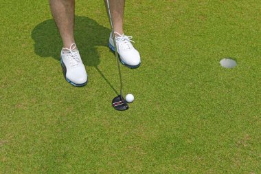 Golf oyuncu beyaz ayakkabılarla bir club golf topu ile bir fincan holding