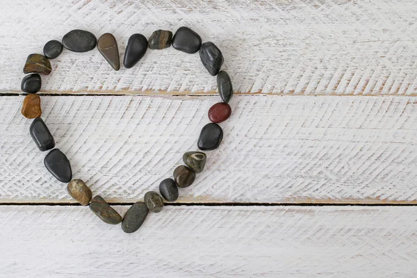 Камень в форме сердца, маленькие камешки расположены в виде сердца на белом деревянном фоне — стоковое фото