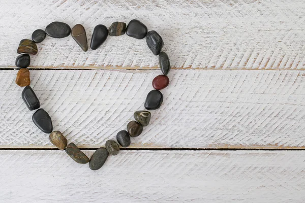 Pierre en forme de coeur, petits cailloux disposés comme un cœur sur fond de bois blanc — Photo