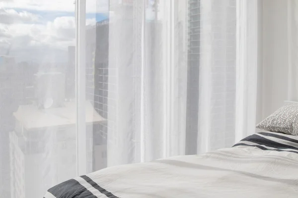 Cama blanca suave y cortina de transparencia con edificios y cielo azul visible —  Fotos de Stock