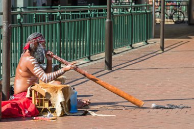 Busker sitting and blowing didgeridoo, Australian Aboriginal wind musical instrument clipart
