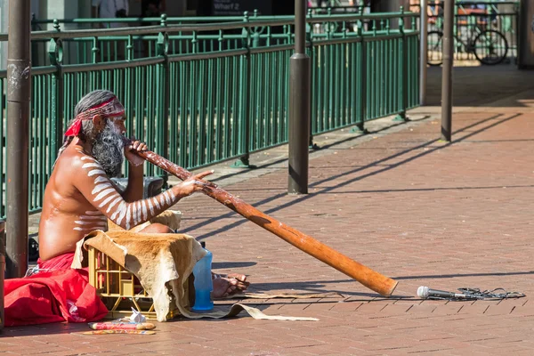 Busker sentado y soplando didgeridoo, australiano aborigen viento instrumento musical — Foto de Stock