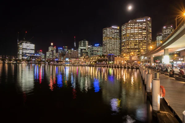 Personas sentadas en el paseo marítimo con vista al horizonte de la ciudad de Sydney por la noche —  Fotos de Stock