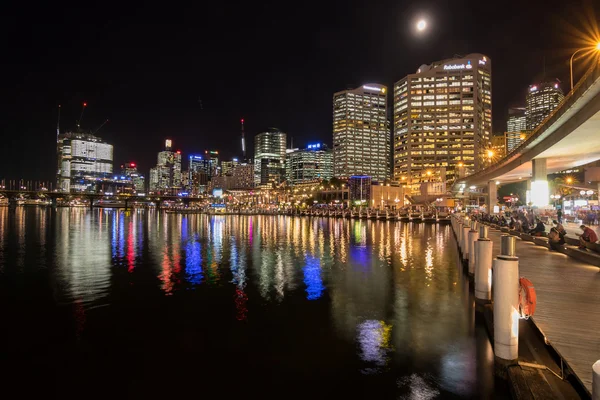 People sitting at harbourside promenade with view of Sydney city skyline at night — Stock Photo, Image