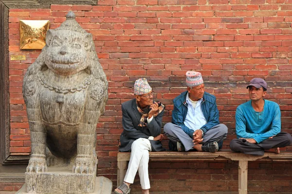 Nepalilaiset miehet istuvat kivileijonan vieressä Patanin museon sisäänkäynnillä Nepalissa. . — kuvapankkivalokuva