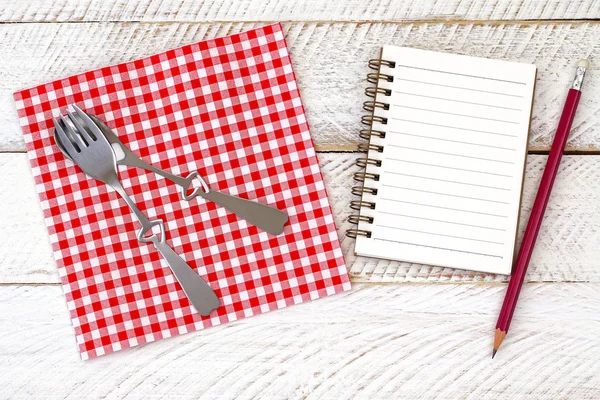 Servilleta de papel con tenedor lindo, cuchara en ella al lado de un cuaderno blanco en blanco —  Fotos de Stock