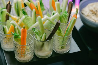 Renkli sebze çubukları bardaklara dizilmiş ve misafirler için kremalı bir sos eşleştirilmiş..