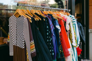 Parlak renkli giysiler güzel bir günde müşterileri çeken modaya uygun bir mağazanın dışındaki ahşap askılarda asılı..
