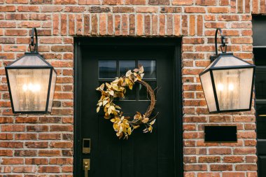 Kapısı siyah, çelengi düşmek üzere olan rahat bir giriş ve tuğla duvara karşı parlayan fenerler..