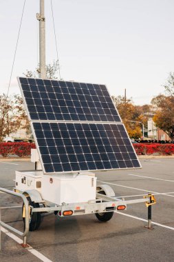 Bir güneş enerjisi römorku boş bir alana park edilmiş, akşamları güneş ışığını ve uzaktaki ağaçları yakalıyor..