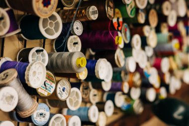 Çeşitli iplik makaraları farklı renklerde bir zanaat atölyesinin duvarında asılı, projeler için hazır..