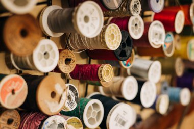 Duvarda farklı renklerde iplik makaraları sergileniyor, el işi ustaları için dikiş malzemeleri sergileniyor..