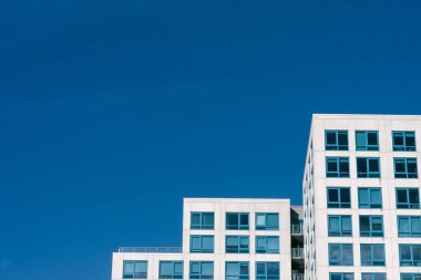 Açık mavi gökyüzüne karşı yükselen iki çağdaş bina, kentsel bir ortamda güneş ışığını yansıtıyor..