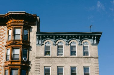 İki farklı tuğla bina, şehir manzarasında parlak mavi bir gökyüzüne karşı mimari özellikler sergiliyor..