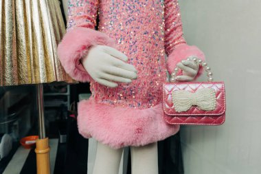 Parlak pembe bir elbise giymiş renkli bir manken dükkanın penceresinin yanında şirin bir el çantası tutuyor..