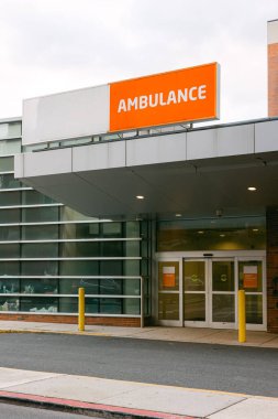 Burası bulutlu bir günde modern bir tıbbi tesisin önünde parlak turuncu bir ambulans işareti içeriyor..