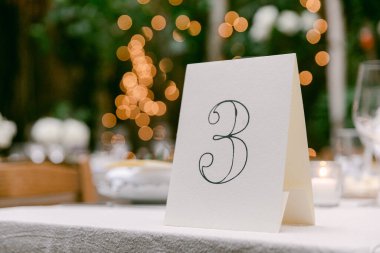 Bahçe ortamında ışıldayan ışıkların arasında üç numaralı kartın olduğu güzel bir masa..