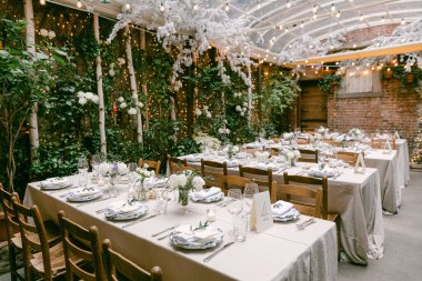 Masalar güzel düzenlenmiş beyaz çiçekler ve dekorasyonlarla büyüleyici bir bahçe düzeninde, toplanmak için mükemmel..