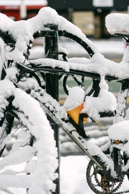 Bir bisiklet, kışın şehirde bir caddede kalın karla kaplı bir askıda park halindedir..