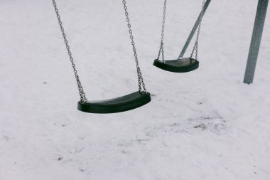 İki salıncak bir parkta sallanıyor, yerde kar var, bir kış günü sakin bir sahne gösteriliyor..