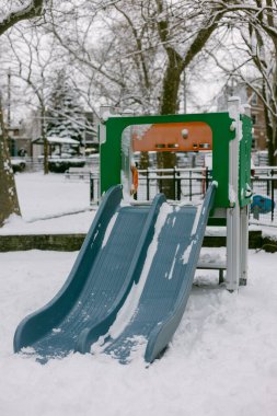 Kar, çocuklar bir kış günü bir parkta oynarken oyun parkı ekipmanlarını kaplıyor..