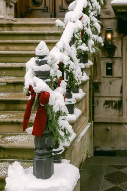 Kar kürkleri dekoratif yeşillik ve kırmızı kurdeleler bir merdivende, bir şehirde kış ve tatil hazırlıklarını sergiliyor..