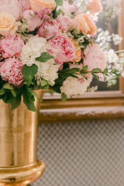 Pembe ve turuncu tonlarda parlak çiçekler arkasında çerçeve olan uzun bir vazoda sergilenir..