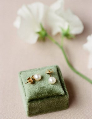 İnci küpeler yeşil bir kutunun üzerinde durur. Arka planda beyaz çiçekler var, basit bir ayar oluşturuyor.