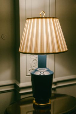 Geleneksel dekorları ve detaylı duvarları olan bir odada bir lamba, masanın üzerine oturur..